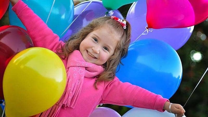 Smiling girl in pink top, surrounded by colourful balloons